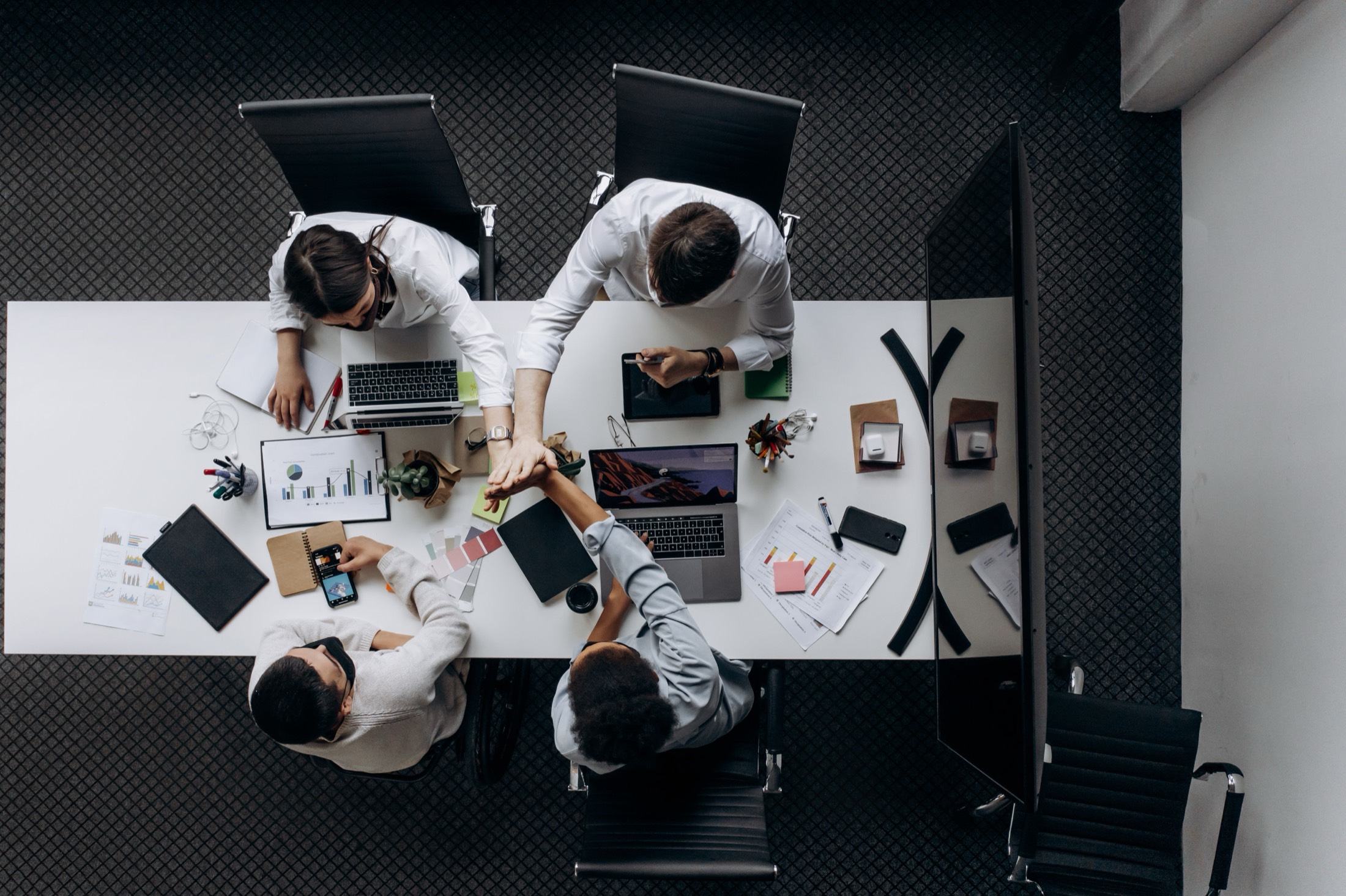 Team high-fiving over a desk covered in charts and laptops